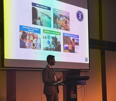 ITOPF presenter wearing grey suit in front of projection screens with ITOPF slides projected on